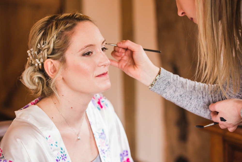 Makeup artist applying bridal makeup and eyeshadow to the bride on her wedding morning.